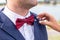 Bride helps the groom to adjust pull the red bow-tie