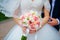 Bride hold groom by the hand and wedding bouquet. Focus on wedding flower bouquet. Crop by chest and legs. Bride in wedding dress