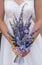 Bride holds elegant wedding bouquet of purple flowers and herbs