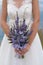 Bride holds elegant wedding bouquet of purple flowers and herbs