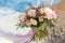 The bride holds a pink and lilac wedding bouquet in her arms against the background of the sea