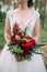 Bride holds wedding bouquet with red flowers