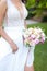 Bride keeping bouquet of flowers and walking in grass background.