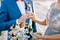 Bride in a lace dress puts an engagement ring on the finger of a groom in a blue suit. Close up