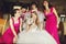 Bride lloks funny while bridesmaids in pink dresses hold her veil