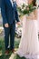 Bride in a long dress with a bouquet stands by the hand with groom in a blue plaid suit