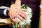 The bride put her hand on her husband`s hand with wedding rings . The newlyweds put their hands on a engagement white bouquet of