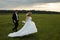 Bride runs on the green field while groom follows her