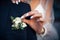 Bride`s hand touches the buttonhole on the groom`s jacket, close-up. Stylish suit, boutonniere of fresh flowers, woman`s hand