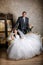 Bride sits in a chair and the groom stands near groom in the room with a beautiful interior