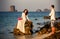 Bride sits on rock groom stands on beach