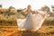 Bride on a summer field in white wedding dress rolling and dancing in sunset light