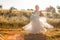 Bride on a summer field in white wedding dress rolling and dancing in sunset light
