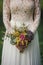Bride wearing lace dress and holding rustic bouquet.