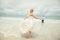 Bride in wedding dress runs to bridegroom over sea turning back. lucky woman on the beach.