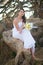 Bride in the wedding dress sits on the roots of a tree in the middle of the stones