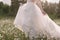 A bride in a wedding dress at sunset walks along a chamomile field in Altai