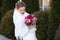 Bride in a white coat posing outdoors, holding a bright bouquet of flowers in her hands. The girl lowered her eyes and