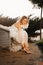 a bride in a white delicate dress adjusts shoes on a chair in park at sunset.