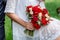 Bride in white dress holding in hands delicate, expensive, trendy bridal wedding bouquet of flowers in marsala and red colors. Clo