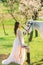 Bride in white dress stands near horse in spring blooming garden