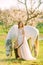 Bride in white dress stands near horse in spring blooming garden