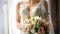 a bride in a white wedding dress, captured in a close-up image, with a delicate bouquet of flowers, standing by the