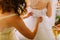 Bridemaiden helps dressing bride her white wedding dress