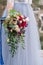 The brides hand holds a wedding bouquet of roses and feverweed on the background of a wedding dress