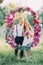 The bridesmaid and the best man are posing through the wedding flower arch in the sunny field.