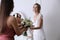 Bridesmaid giving bouquet to beautiful woman in wedding dress indoors