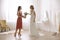 Bridesmaid giving bouquet to beautiful woman in wedding dress indoors