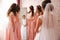 Bridesmaid standing by the mirror and help bride look at yourself. Big mirror at home. Happy girl`s in same dress