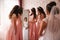 Bridesmaid standing by the mirror and help bride look at yourself. Big mirror at home. Happy girl`s in same dress