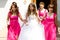 Bridesmaids in pink dresses hold bride\'s arms walking out of the