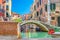 Bridge across narrow water canal in Venice with moored boats between old colorful buildings with balconies