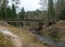 Bridge over a small wild river, with many bends, beautiful conifers overgrown river banks, autumn time in nature