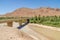 Bridge spanning over dry river bed with some water, mountains and palms in Morocco, North Africa