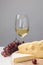 Brie and maasdam cheese on wooden board, white wine glass and grapes on gray