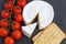 Brie soft cheese with crackers and tomato on a grey slate boar