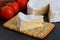 Brie soft cheese with crackers and tomato on a grey slate boar