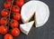 Brie soft cheese with tomato on a grey slate board.