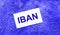 On a bright blue abstract background, there is a white card with the text IBAN International Bank Account Number