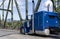 Bright blue classic American idol big rig bonnet semi truck tractor running on the arched truss bridge at sunny day