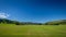 A bright blue sky above a pristine cricket ground surrounded by rolling hills
