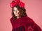 A bright and bold young woman with roses on her head and a red knitted cape.