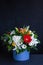 Bright bouquet of gerberas, chrysanthemums, lilies, green leaves in a gift box on a dark background. Selective focus