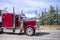 Bright burgundy classic bonnet American big rig semi truck with stylish chrome parts transporting cargo in refrigerator semi