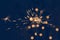 Bright burning sparkler with flying sparks. Dark blue background with blurred lights of Christmas garland.