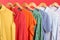 Bright clothes on hangers against red, closeup. Rainbow colors